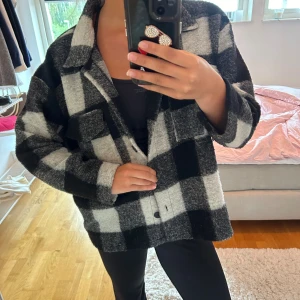 Svartvit rutig overshirt jacka - Säljer en oversized svartvit rutig overshirt jacka med stora knappar framtill och bröstficka. Jackan har en mjuk och lite fluffig känsla, perfekt för lager-på-lager. Passar dig som gillar streetstyle och chill vibe.