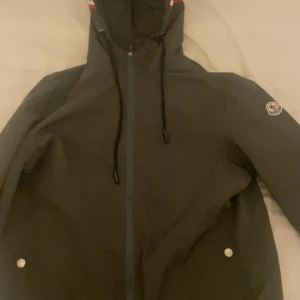 Svart vindjacka från Moncler - Snygg svart vindjacka från Moncler med huva och svarta snören. Jackan har dragkedja framtill, två fickor med tryckknappar och Moncler-logga på vänster ärm. Perfekt för dig som gillar stilren design och sportig vibe.Skriv för mer info och bilder!!😆