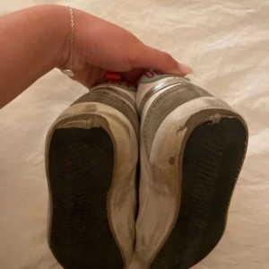 Golden Goose Mid Star sneakers grå/vit - Säljer ett par Golden Goose Mid Star åt min tjej i vitt och grått med silverdetaljer och stjärna på sidan. Skorna har snörning med text på skosnörena, ljusblå hälkappa med röd 'GOLDEN'-text och orange flärp. Ovandel i skinn och mocka, platt sula och rund tå. Bilderna kan se lite dåliga ut men skriv till mig om ni vill ha några fler eller undrar över något 