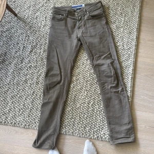 Beige jeans från Jacob Cohën - Snygga beige jeans från Jacob Cohën med klassisk femficksdesign och raka ben. Byxorna är tillverkade i bomull och har knäppning framtill med märkets logga på knapparna. Stilsäkra och italiensktillverkade, perfekta för en clean look.