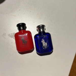 Ralph Lauren Polo parfymset - Snyggt parfymset från Ralph Lauren med två flaskor: en röd och en blå, båda i glas med klassiska Polo-loggan i silver. Flaskorna har rundade former och svarta respektive silvriga korkar. Perfekt present till någon som gillar stilrena dofter. 