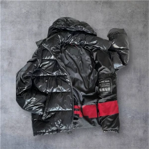 Svart pufferjacka från Michael Kors - Säljer en glansig svart pufferjacka från Michael Kors med röda detaljer på insidan. Jackan har huva, dragkedja och är perfekt för kalla dagar. Stilsäker och riktigt skön att bära när det är kyligt ute.