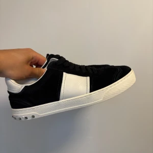 Valentino flycrews sneakers svart/vit - Svarta och vita Valentino Flycrews sneakers i mocka och skinn med coola nitar på hälen. Klassisk låg modell med snörning, svart ovandel i mocka och vita detaljer i skinn. Snygg kontrast mellan färgerna och exklusiv känsla. (Alla nitar kvar)(39 fits 40-41)