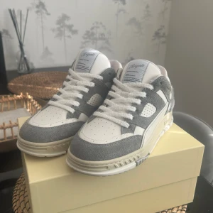 Axel Arigato Area Lo Fluffy grå/vita sneakers strl 40 -  Snygga sneakers från Axel Arigato i grå mocka och vitt skinn. Klassisk låg modell med rund tå, perforerade detaljer och tjock vit sula. Skorna har vita snören och märkning på sidan av sulan. Perfekta för dig som gillar stilrena och trendiga sneakers. Säljes då jag efter ett par timmar insåg att dem är lite för små för mig, använda i ett par timmar utomhus, så gott som nya. NYPRIS 3080kr! Kvitto finns!