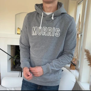 Grå hoodie från Morris  - Säljer en grå hoodie från Morris med vit broderad logga på bröstet tröjan är i nytt skick och de finns bara ett limiterat antal. Tröjan har huva med snörning, magficka och långa ärmar. Mjuk och skön bomullsmix som passar perfekt till jeans. Snygg och enkel stil för dig som gillar klassiska hoodies. Storlek L men passar även M