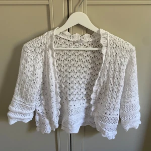 Vit stickad bolero med spetskant - Superfin vit stickad bolero med vacker spetskant och trekvartsärm. Aldrig använd!