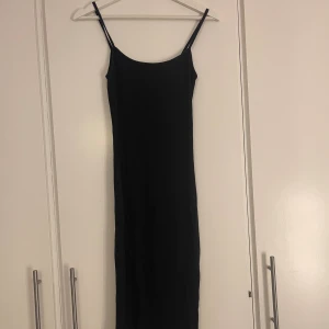 Svart långklänning från Amisu - Svart ribbad långklänning från Amisu med smala axelband och figurnära passform. Klänningen är ärmlös och har en enkel, stilren design som är lätt att matcha med olika accessoarer. Materialet är mjukt och stretchigt för en bekväm känsla.