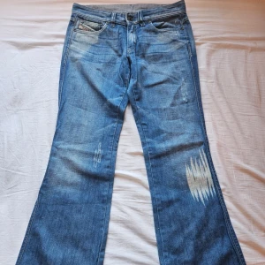 Blå bootcut jeans från Diesel - Säljer ett par blå bootcut jeans från Diesel med slitna detaljer och snygg tvätt. För att jag fick dom utan att testa och dom var för små. Klassisk femficksmodell med logga på myntfickan. Jeansen har bredare ben nertill och coola slitningar framtill för en avslappnad look.