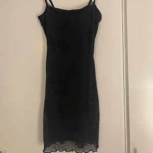 Svart kort klänning - Säljer en svart kort klänning från H&M i storlek XXS. Klänningen har smala axelband och är figurnära med lätt transparent mesh och subtilt mönster. Perfekt för dig som gillar minimalistisk stil med en twist.