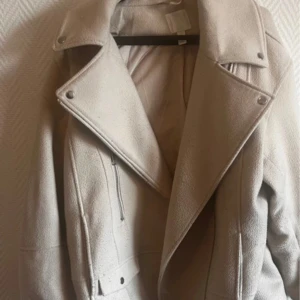 Beige ull bomberjacka med dragkedja - Snygg beige bomberjacka i ull med bred krage och coola detaljer som silverfärgade dragkedjor och tryckknappar. Jackan har en rak passform och är långärmad, perfekt för dig som gillar stilrena och neutrala plagg. Det är storlek S men den är stor i storlek, jag skulle säga att den passar upp till M/L