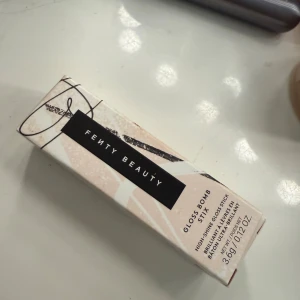 Fenty Beauty Gloss Bomb Stix Blaz’d Donut - Fenty Beauty Gloss Bomb Stix i färgen Blaz’d Donut 01. Ett high-shine gloss stick med nude-rosa ton, perfekt för att ge läpparna en glansig finish. Kommer i en snygg, stilren förpackning med 3,6g produkt.