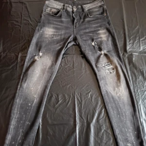 Svarta Dsquared2 jeans med slitningar - Snygga svarta jeans från Dsquared2 med coola slitningar och färgstänk för en edgy look. Jeansen ör i gott skick