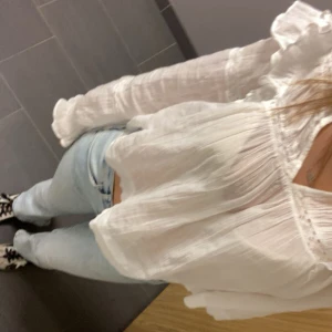 Vit blus med volang Gina! - Säljer en luftig vit blus med volangdetaljer på axlarna och spets längs bröst och ärmslut. Blusen är croppad och har långa ärmar med lätt puff och rynkade muddar. Perfekt för dig som gillar romantisk och bohemisk stil.