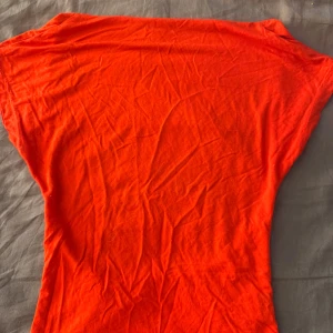 Röd tshirt  med öppen rygg - Säljer en snygg röd tshirt i mjuk bomull. Toppen har en cool öppen rygg och korta ärmar. Perfekt för dig som vill sticka ut med en stark färg och enkel design.