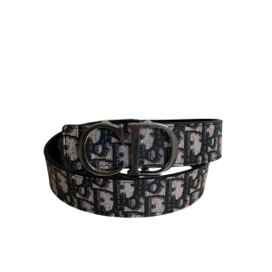 Svart och vit Dior bälte med logomönster - Snyggt bälte från Dior med ikoniskt svart och vitt logomönster och en stor, silverfärgad CD-spänne framtill. Bältet är tillverkat i skinn och har en modern, stilren look som lyfter vilken outfit som helst.