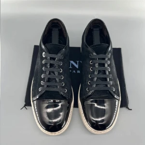 Svarta sneakers med lackad tå - Snygga svarta sneakers från Lanvin med cool kontrast mellan mocka och blank lackad tå. Skorna har vita sulor och svarta skosnören. Perfekta för dig som gillar stilrena men ändå unika detaljer. Passar till många olika outfits.