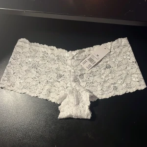 Vita spets-hipsters i blommig design - Säljer ett par vita oanvända hipster-trosor i bred spets med blommigt mönster. Storlek M.