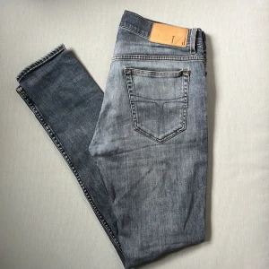 Grå slim jeans Tiger of Sweden - Slim fit jeans från Tiger of Sweden i en snygg grå tvätt. Klassisk femficksmodell med läderpatch bak i midjan och diskreta kontrastsömmar. Tillverkade i Italien och perfekta för dig som gillar stilrena och moderna jeans.
