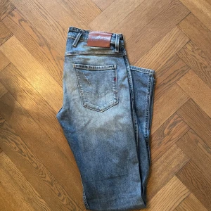 Replay Jeans  - Snygga Replay Anbass jeans i ljusblå tvätt med slitna detaljer och slim fit. Klassisk femficksmodell med Replay-logga på fickan och läderpatch bak. Jeansen är tillverkade i bomull och har en modern, smal passform som sitter riktigt bra.