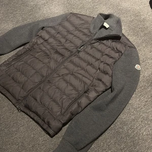 Moncler cardigan  - Snygg grå moncler cardigan från Moncler med quiltad framsida och stickade ärmar. Jackan har dragkedja framtill, två fickor med dragkedja och Moncler-logga på ärmen. Perfekt för kyliga dagar och ger en clean, modern look. Inget kvitto följer med men det är legit checkad så den är äkta.