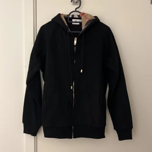Svart burberry zip hoodie - Svart zip hoodie från burberry. Av någon anledning var den extremt liten i storleken så XL sitter som S av någon anledning. Säljer eftersom den var för liten. Helt oanvänd. Pris kan diskuteras, tar ej byten. Ja den är äkta.