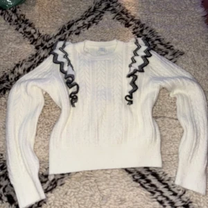 Stickad vit tröja med svart vita volanger - Stickad vit tröja med svart/vita volanger. Bra skick i storlek: S