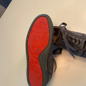 Christian Louboutin sneakers med nitar - Säljer ett par mörkgrå sneakers från Christian Louboutin med ikonisk röd sula och coola nitar på tån  vid snabb affär så är 1064kr okej men inte lägre än så