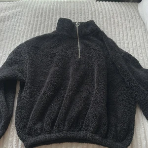 Svart fleece-tröja med half zip - Mysig svart fleece-tröja med hög krage och half zip-dragkedja framtill. Tröjan har lång ärm och är tillverkad i fluffigt, mjukt fleecematerial som håller dig varm under kyliga dagar. Perfekt för lager-på-lager och chill dagar.