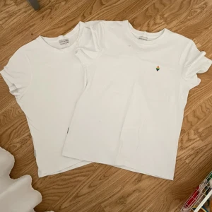 Vita t-shirts från ARKET - Två vita t-shirts från panos i klassisk modell med rund hals och kort ärm. Den ena har en liten broderad regnbågsfärgad detalj på bröstet. Perfekta basplagg till garderoben och gjorda i mjuk bomull.