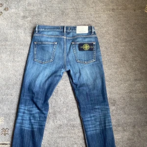 Stone Island Jeans - Blå jeans från Stone Island med klassisk femficksdesign, slitna detaljer vid myntfickan och ikonisk Stone Island-patch på bakfickan. Jeansen har orange kontrastsömmar och en snygg tvättad look. Perfekt för dig som gillar streetwear och vill sticka ut. Storlek: W30 L32 ‼️Kan gå ner i pris vid snabb affär‼️