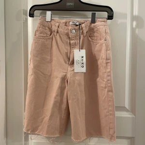 Dusty pink jeansshorts från NA-KD - Långa jeansshorts i en snygg dusty pink färg från NA-KD. Modellen har hög midja, råa kanter nertill och klassisk femficksdesign. Perfekta för en chill och trendig look i sommar. Materialet är denim i bomull.