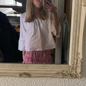 Vit blus med broderade ärmar - Säljer en luftig vit blus med v-ringning och trekvartsärmar. Ärmarna har fina broderade detaljer och lätt volang vid avslutet. Blusen är i bomull och har en avslappnad passform, perfekt till jeans eller kjol.