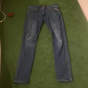 Replay Anbass blå jeans, W29 L32 - Snygga blå Replay Anbass jeans med klassisk femficksdesign och diskreta slitningar. Jeansen har raka ben och normal passform, med tydliga kontrastsömmar och Replay-logga på myntfickan. Perfekta för dig som gillar stilrena och bekväma jeans med en grich och rik still 🍾🍾🔥🔥🔥🔥