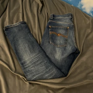 ljus Blå Nudie Jeans - Snygga ljus blå jeans från Nudie med tydliga orange sömmar på bakfickorna. Klassisk femficksmodell med rak passform och normal midja. Jeansen har en cool tvättad look och är tillverkade i robust denim.