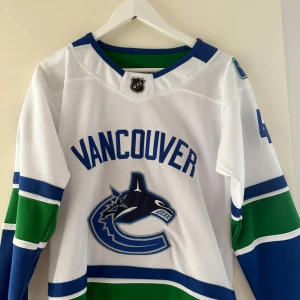Vancouver Canucks Pettersson tröja - Säljer en Vancouver Canucks NHL-tröja med Pettersson #40 på ryggen. Tröjan är vit med blå och gröna detaljer, långärmad och har broderat lagmärke på bröstet. Adidas-logga på ryggen och NHL-märke vid halsen. Perfekt för dig som älskar hockey och vill representera ditt favoritlag. Priset går att diskutera 