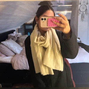 Beige stickad halsduk i mjukt material - Säljer en stor och mysig beige stickad halsduk som är perfekt att svepa runt halsen. Den har en enkel och stilren design utan mönster och är gjord i ett mjukt material som känns skönt mot huden. Passar dig som gillar klassiska accessoarer.