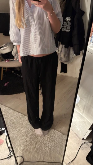 Svarta linnebyxor med snörning - Svarta linnebyxor med avslappnad passform och snörning i midjan. Byxorna har raka ben och är perfekta för dig som gillar en chill och enkel stil. Materialet är linne vilket gör dem sköna och luftiga.