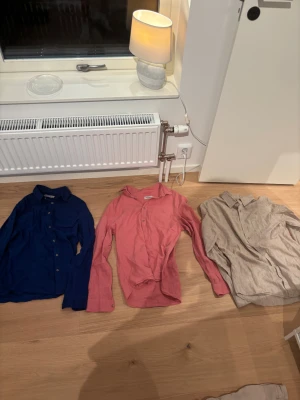 Tre Dressmann linneskjortor i M - Tre skjortor från Dressmann i storlek M, tillverkade i linnemix. En är djupblå, en är beige och en är korallrosa. Alla har klassisk krage, knappar framtill och lång ärm. Perfekt för dig som gillar stilrena och luftiga skjortor med skön passform.