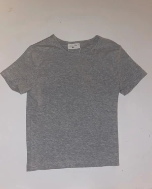 Grå basic tight topp S - En enkel och stilren gråmelerad tight topp med rund halsringning och korta ärmar. Perfekt att matcha med jeans eller kjol för en clean look. Tillverkad i mjukt bomullsmaterial som känns skönt mot huden.