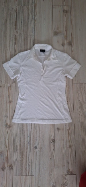 Vit henley från Galvin Green S - Snygg vit henley från Galvin Green i storlek S. Skjortan har korta ärmar, klassisk krage och knappar framtill. Tillverkad i mjuk bomull som andas, perfekt för dig som gillar sportig och clean stil. Golftröja- Passformen är normal och materialet känns riktigt skönt mot huden.