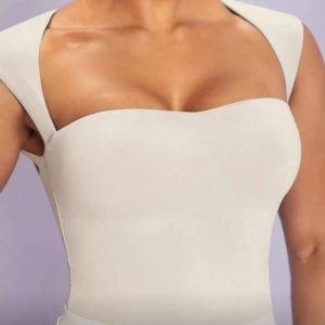 Vit topp med öppen rygg och breda axelband - Snygg vit topp med breda axelband och unik öppen rygg. Toppen har en stilren, figurnära passform och är tillverkad i ett slätt tyg. Perfekt för dig som vill sticka ut med en modern och minimalistisk look.