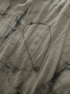 Silverfärgat halsband från Edblad - Stilrent halsband i silverfärg från edblad med tunn kedja och rund berlock med små stenar runt om. Liten bricka med logga vid låset. Perfekt för dig som gillar minimalistiska smycken.