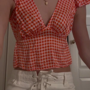 Rutig omlottopp från Topshop - Superfin omlottopp från Topshop i röd och rosa rutigt mönster. Toppen har v-ringning, korta ärmar och lätt utsvängd passform. Perfekt för dig som gillar färg och mönster. Materialet är mjukt och tunt, troligtvis polyester. ❤️🩷