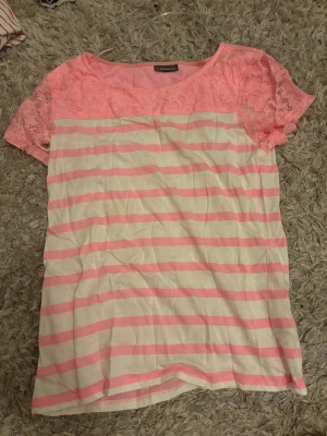 Rosa och vit randig blus med spets - Säljer en söt blus från Street One i storlek 40. Toppen har korta ärmar i rosa spets och en kropp med ljusrosa och vita ränder