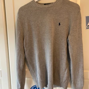 Grå stickad tröja från Polo Ralph Lauren (NY SKICK) - Säljer en klassisk grå stickad tröja från Polo Ralph Lauren med rund halsringning och broderad marinblå logga på bröstet. Inget hål eller fläckar, är i storlek m men sitter som en s. Jätte fint skick, priset ej huggen i sten. Hör bara av dig vid funderingar eller något!!