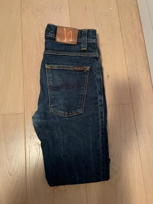 Mörkblå jeans från Nudie Jeans Co - Snygga mörkblå jeans från Nudie Jeans Co med klassisk femficksdesign och orangea kontrastsömmar. Modellen har en slim passform och raka ben, tillverkade i slitstarkt bomullsjeansmaterial. Perfekt för dig som gillar stilrena och tidlösa jeans. Passar dig mellan 172-183 skulle jag säga. Hör av er vid minsta fundering!