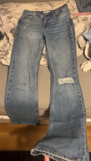 Blå bootcut jeans från Perfect Jeans - Snygga ljusblå jeans från Perfect Jeans i klassisk bootcut-modell. Jeansen har fem fickor, slitning vid ena knät och normal passform. Tillverkade i jeansmaterial med bälteshällor och knappstängning. Perfekt för dig som gillar retrovibe och avslappnad stil. Har även används två gånger efter jag köpt de och sitter väldigt bra. 