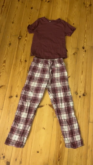 Rutig vinröd mjukisbyxa+tröja strl 146/152 - Mysiga mjukisbyxor i vinrött och vitt med rutigt mönster och snörning i midjan. Byxorna har en loose passform och är tillverkade i mjukt bomullsmaterial, perfekta för chill hemma. Elastisk midja för extra komfort.