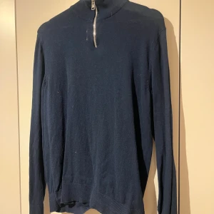 Marinblå stickad polotröja med zip - Snygg marinblå stickad polotröja från Jack and Jones med half zip i silver. Tröjan har långärmad design och ribbade muddar vid ärmslut och nederkant. Perfekt för dig som gillar stilren och enkel look med lite edge.