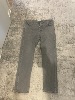 Grå jeans från Jack & Jones - Storlek 32-32                                             Snygga grå jeans från Jack & Jones med klassisk femficksdesign och knappgylf. Jeansen har en rak passform och är tillverkade i slitstarkt denimtyg. Perfekta för dig som gillar en enkel och stilren look.